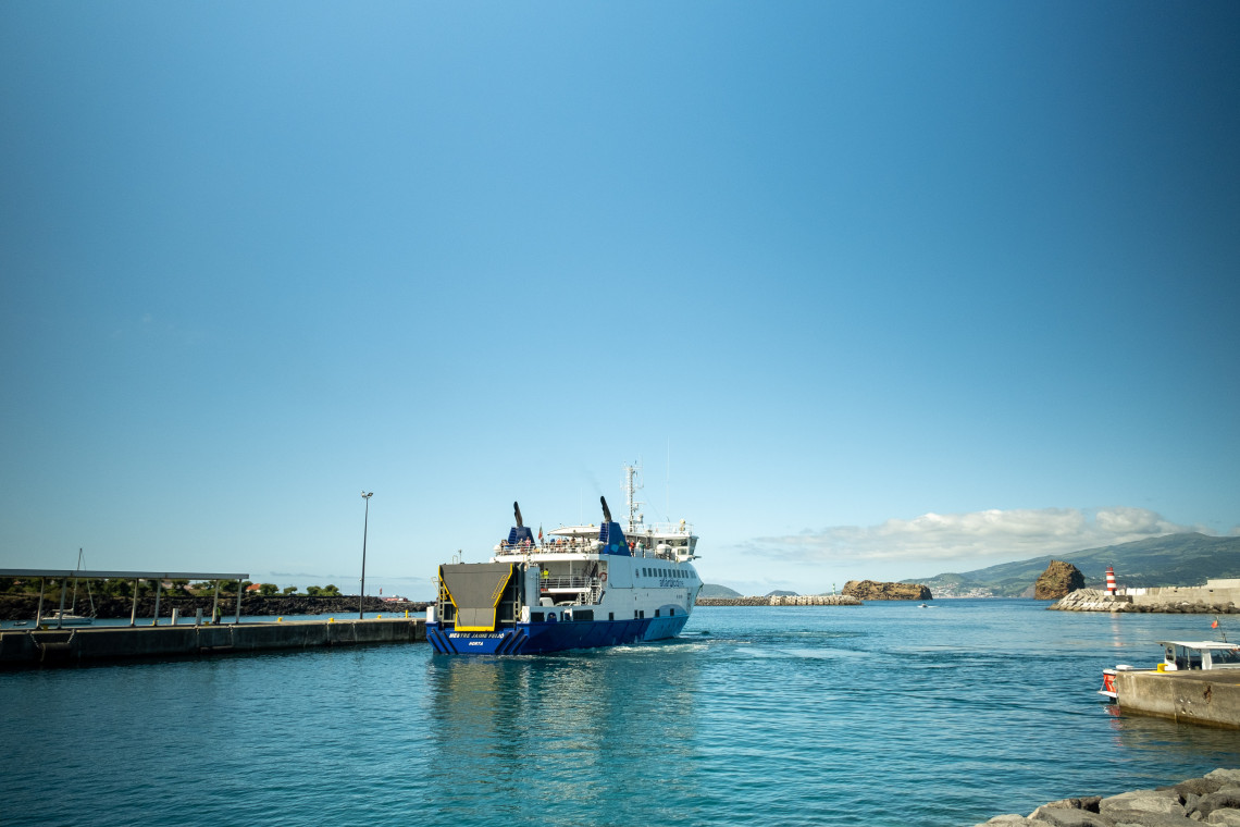 Inter-island ferry docked at the Port of Madalena on Pico Island, with the harbor entrance, volcanic coastline and Faial Island visible across the channel.